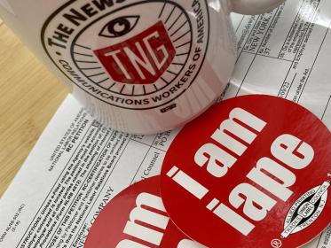 A NewsGuild mug and red stickers with the words I am IAPE